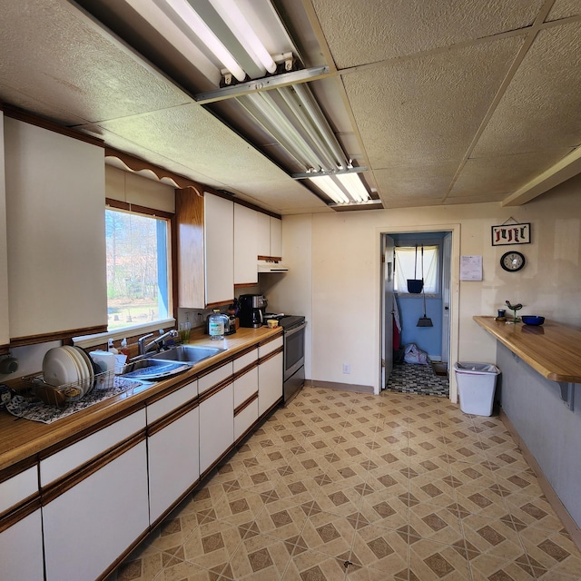 kitchen with sink, stainless steel range with electric stovetop, light tile flooring, and white cabinetry