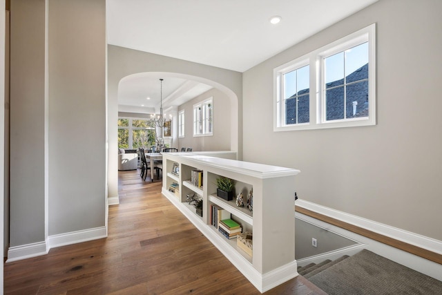 corridor with wood-type flooring, a notable chandelier, and plenty of natural light