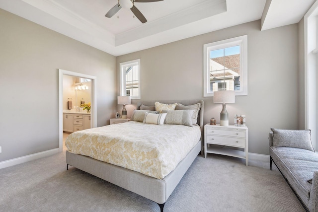 carpeted bedroom with ensuite bathroom, multiple windows, ceiling fan, and a raised ceiling