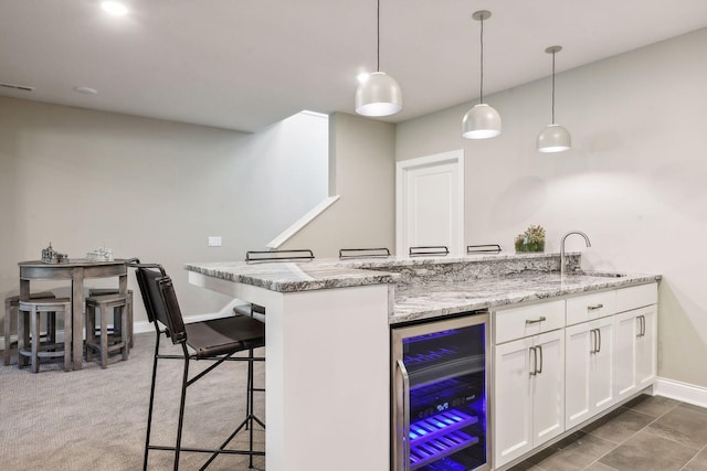 kitchen with decorative light fixtures, wine cooler, sink, kitchen peninsula, and white cabinetry