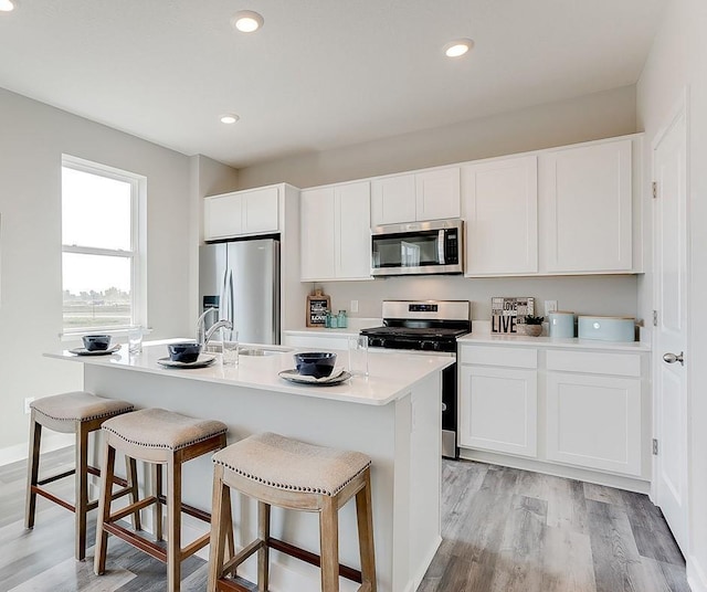 kitchen featuring appliances with stainless steel finishes, an island with sink, light hardwood / wood-style floors, white cabinets, and a breakfast bar