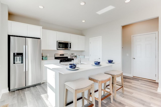 kitchen with white cabinets, appliances with stainless steel finishes, light hardwood / wood-style flooring, and a kitchen island with sink