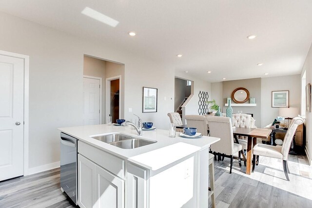 kitchen with an island with sink, sink, light wood-type flooring, stainless steel dishwasher, and white cabinets