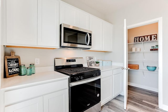 kitchen with appliances with stainless steel finishes, white cabinets, and light hardwood / wood-style floors