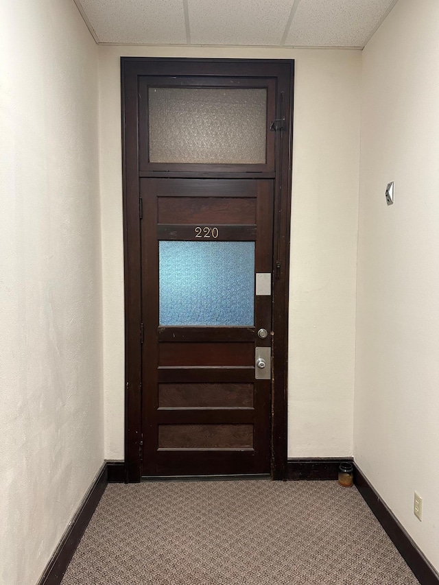 entryway featuring dark colored carpet and a drop ceiling