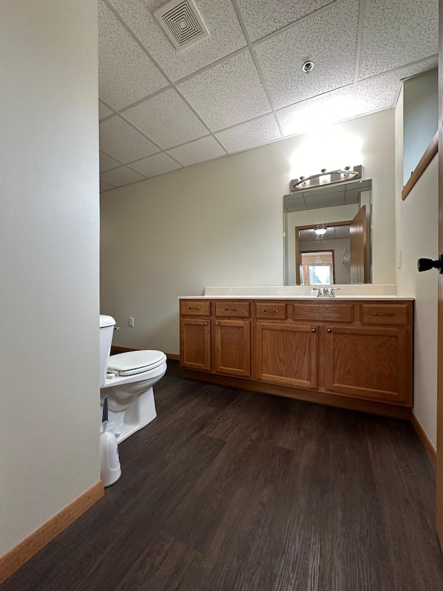 bathroom with hardwood / wood-style floors, vanity, toilet, and a drop ceiling