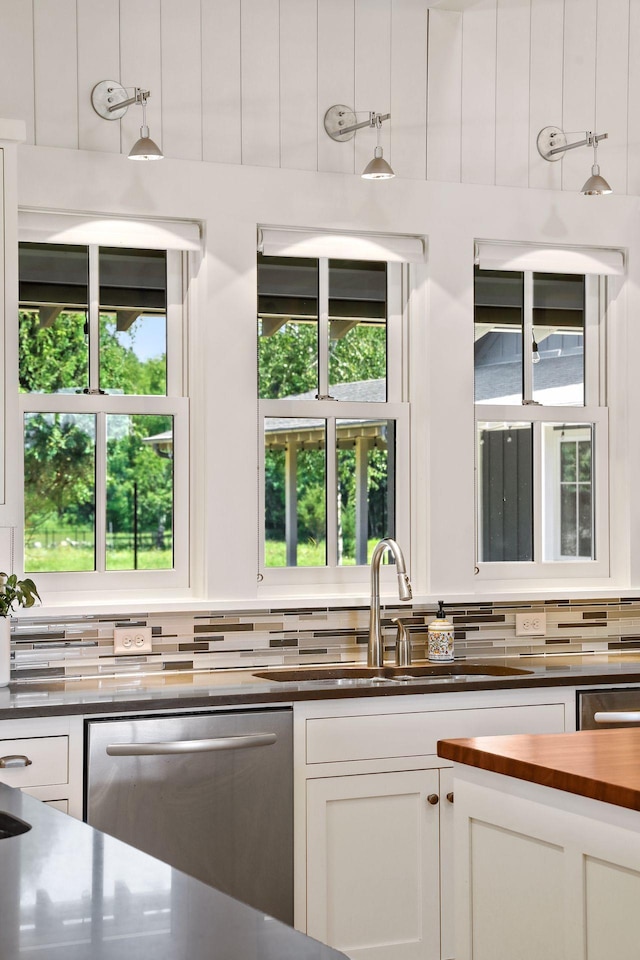 kitchen with a healthy amount of sunlight, tasteful backsplash, white cabinets, and stainless steel dishwasher