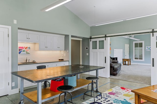 kitchen with high vaulted ceiling, white cabinetry, a barn door, sink, and tasteful backsplash