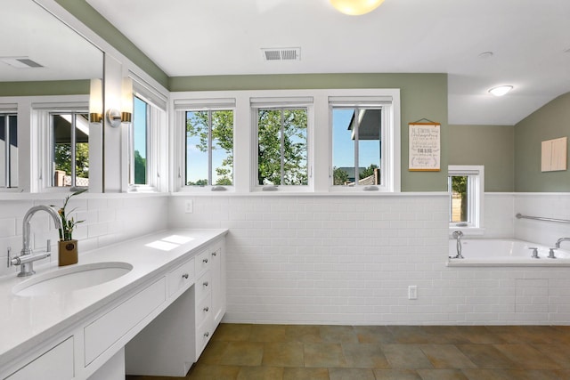 bathroom featuring tile flooring, plenty of natural light, vanity with extensive cabinet space, and tiled tub