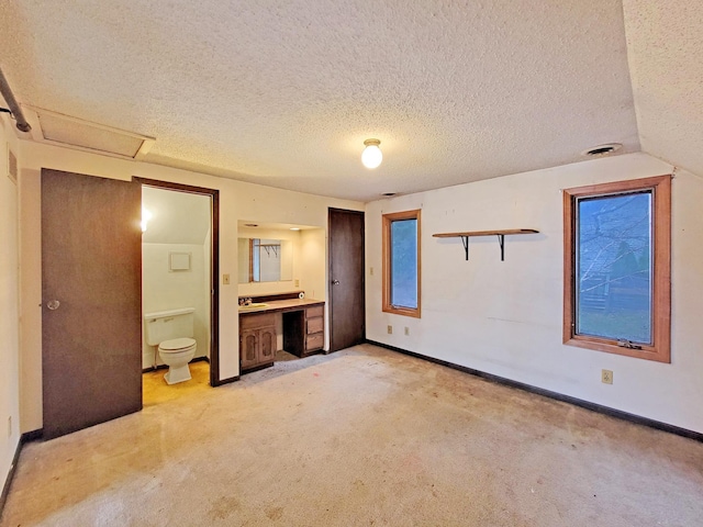 unfurnished bedroom featuring a textured ceiling, lofted ceiling, ensuite bath, and light carpet