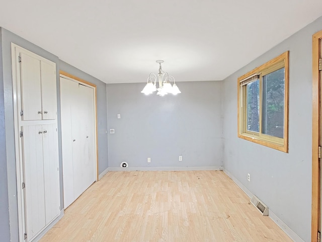 unfurnished room with a notable chandelier and light wood-type flooring