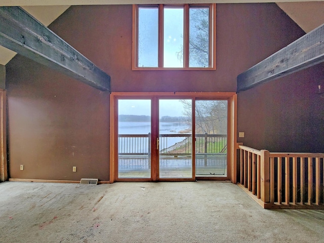 unfurnished living room featuring carpet floors, a water view, and a high ceiling