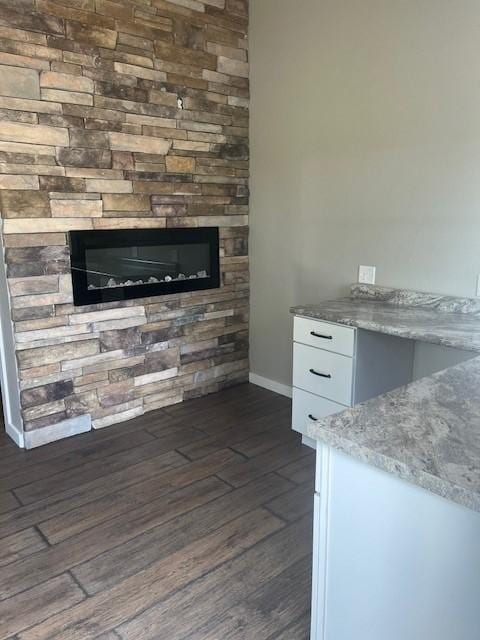 interior space featuring white cabinets, dark hardwood / wood-style floors, light stone counters, and a stone fireplace