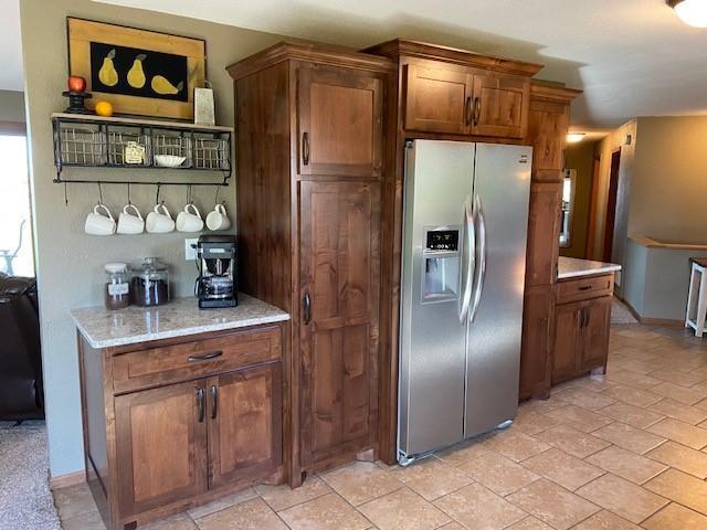 kitchen with light tile flooring, stainless steel fridge, and light stone counters