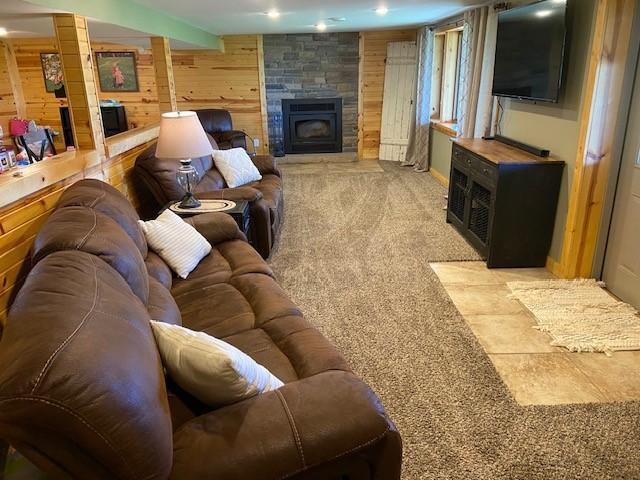 carpeted living room with a fireplace and wooden walls