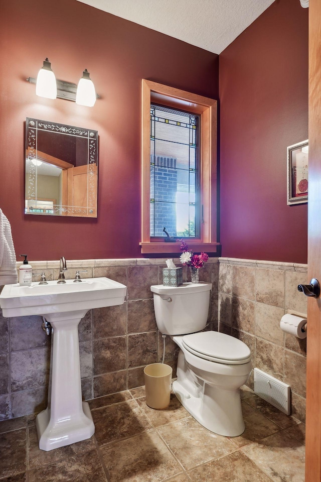 bathroom with a textured ceiling, tile walls, and toilet