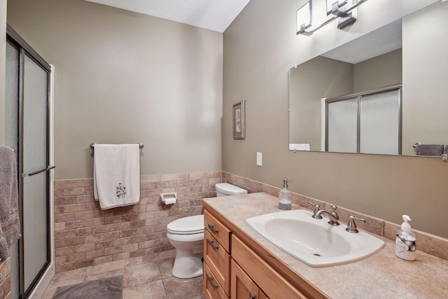 bathroom with tile walls, vanity, toilet, and a shower with shower door