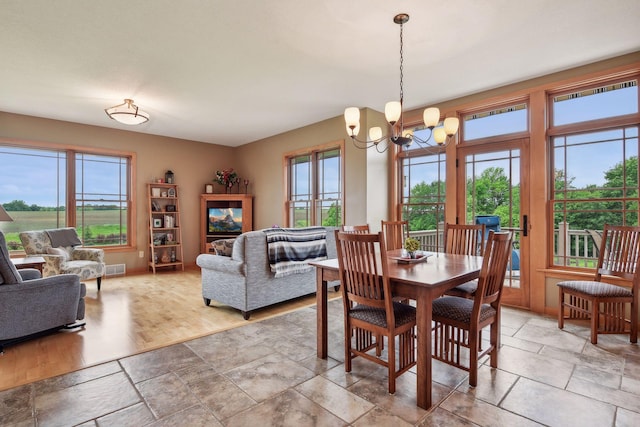 dining space with a notable chandelier, light wood-type flooring, and a healthy amount of sunlight