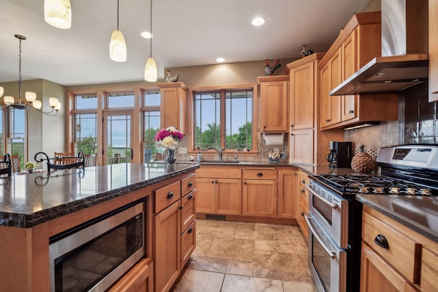 kitchen featuring tasteful backsplash, wall chimney exhaust hood, stainless steel appliances, an inviting chandelier, and decorative light fixtures