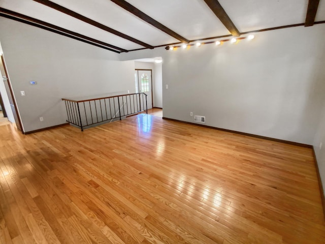 empty room featuring beamed ceiling and light hardwood / wood-style floors