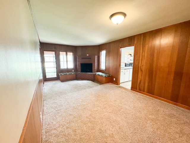 unfurnished living room featuring a brick fireplace, light carpet, and wooden walls