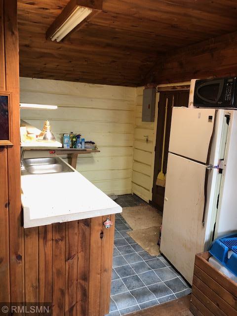 kitchen with electric panel, wood walls, wooden ceiling, and white refrigerator