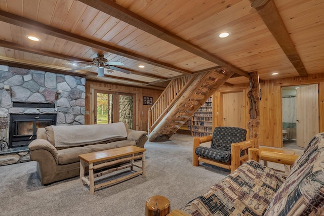 living room with wooden walls, a stone fireplace, carpet, and beam ceiling