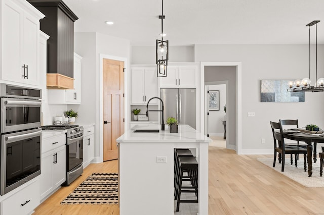 kitchen featuring decorative light fixtures, light wood-type flooring, appliances with stainless steel finishes, sink, and a center island with sink