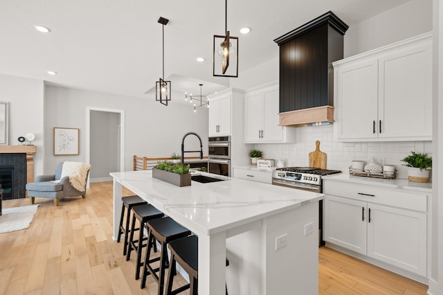 kitchen with appliances with stainless steel finishes, light hardwood / wood-style flooring, tasteful backsplash, a center island with sink, and premium range hood