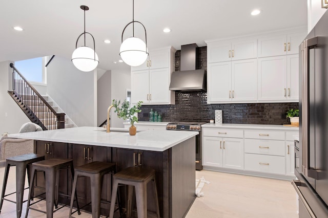 kitchen with appliances with stainless steel finishes, backsplash, a breakfast bar area, wall chimney exhaust hood, and pendant lighting