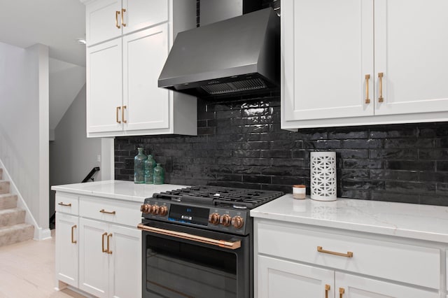 kitchen with white cabinets, high end black range, wall chimney exhaust hood, and light stone counters