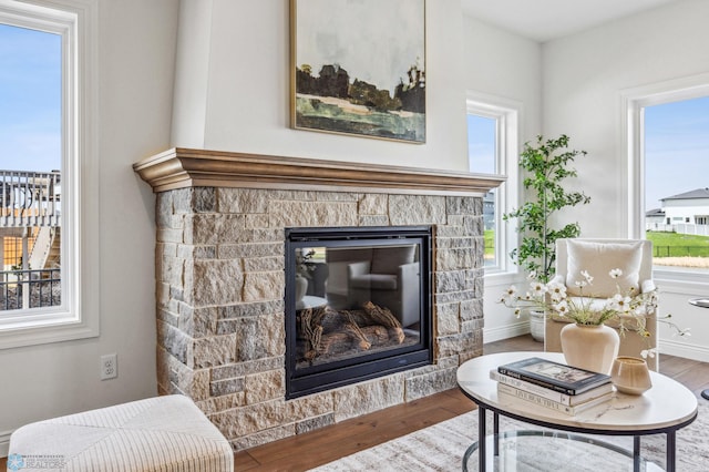 living area with a stone fireplace, plenty of natural light, and hardwood / wood-style floors