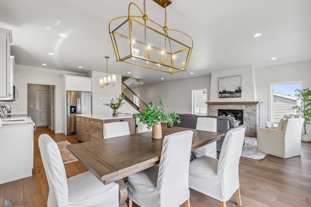 dining area with a stone fireplace, a chandelier, sink, and light hardwood / wood-style flooring