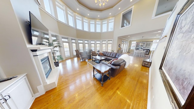 living room featuring a fireplace, light hardwood / wood-style floors, a high ceiling, a notable chandelier, and ornamental molding