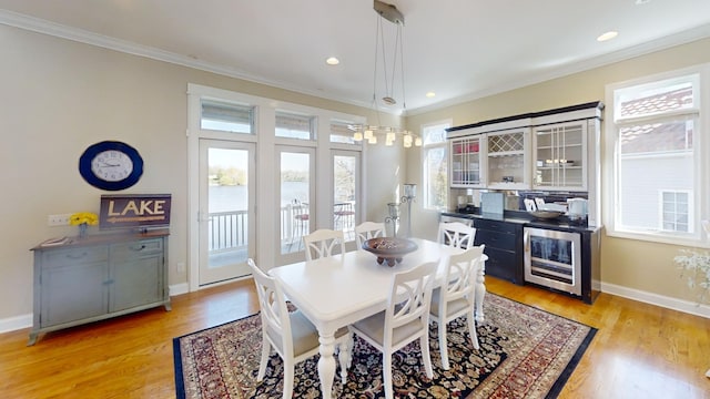 dining space featuring beverage cooler, light hardwood / wood-style floors, crown molding, and a wealth of natural light