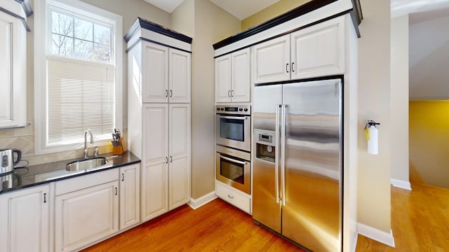 kitchen featuring appliances with stainless steel finishes, sink, decorative backsplash, light wood-type flooring, and white cabinetry