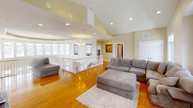 living room with a notable chandelier, a wealth of natural light, a raised ceiling, and light wood-type flooring