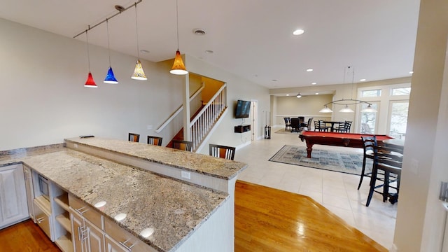 kitchen featuring billiards, hanging light fixtures, rail lighting, light stone countertops, and kitchen peninsula