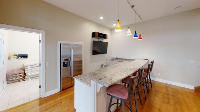 kitchen with light wood-type flooring, high end fridge, light stone countertops, hanging light fixtures, and a kitchen bar