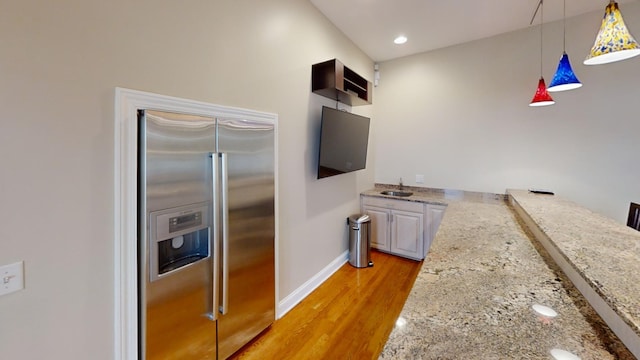 kitchen with pendant lighting, high end refrigerator, light hardwood / wood-style flooring, and light stone counters