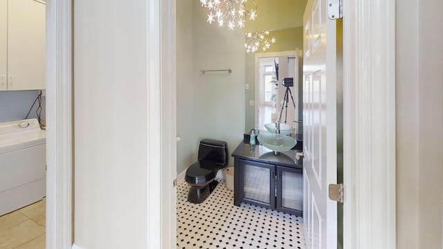 bathroom with an inviting chandelier, toilet, tile patterned floors, washer / dryer, and sink