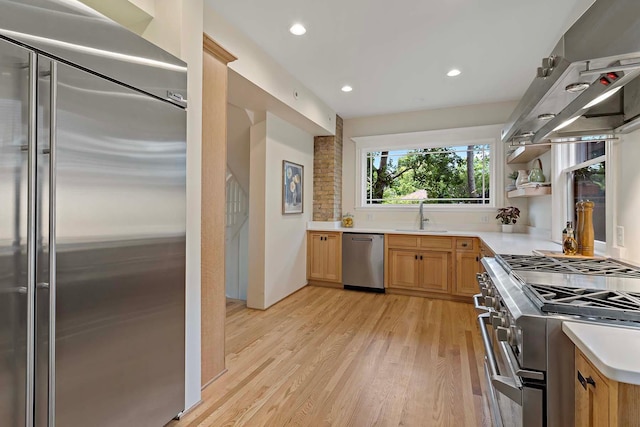 kitchen with high end appliances, sink, extractor fan, light wood-type flooring, and light brown cabinetry