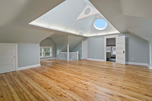 additional living space featuring vaulted ceiling with skylight and light hardwood / wood-style flooring