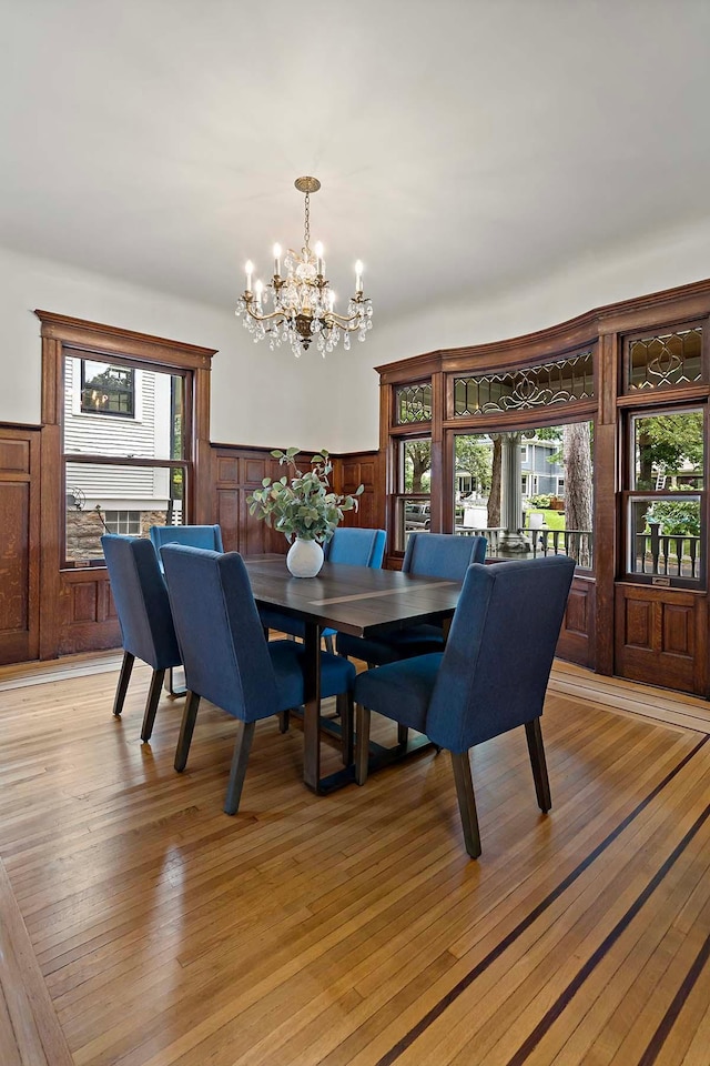 dining area with a chandelier, wooden walls, and light wood-type flooring