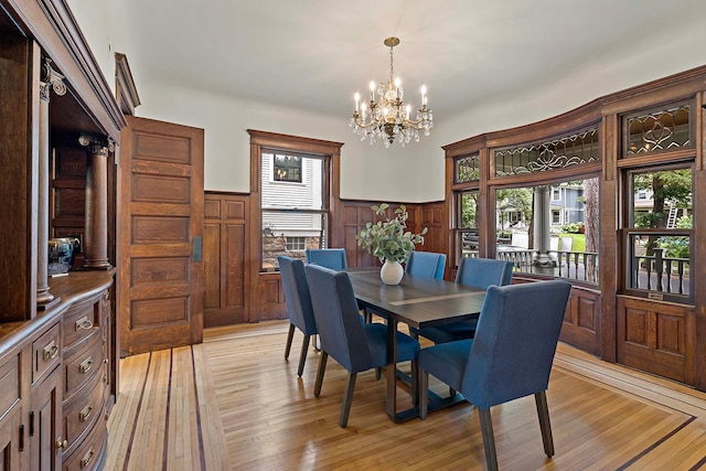 dining space featuring light hardwood / wood-style flooring, wooden walls, and a chandelier