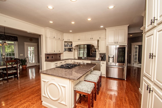 kitchen featuring a kitchen island, dark hardwood / wood-style floors, hanging light fixtures, appliances with stainless steel finishes, and a kitchen bar