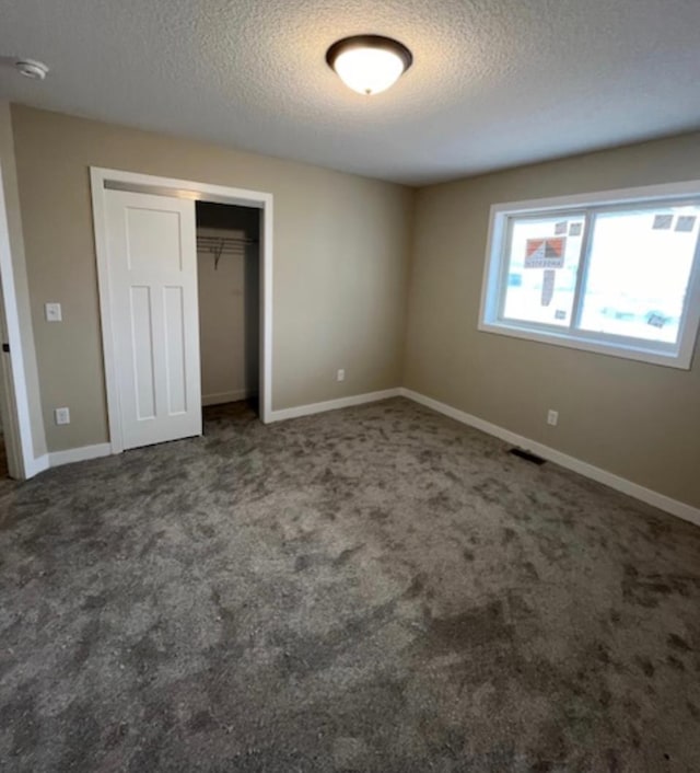 unfurnished bedroom with a closet, a textured ceiling, and dark carpet