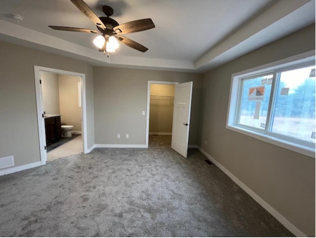 unfurnished bedroom featuring a spacious closet, a tray ceiling, ceiling fan, connected bathroom, and light colored carpet