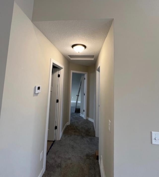 corridor with a textured ceiling and dark colored carpet