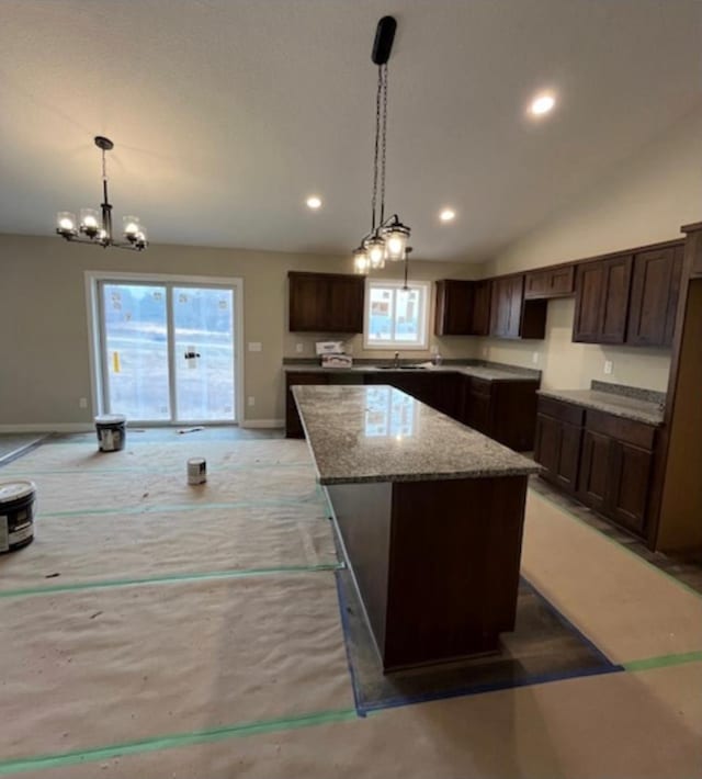 kitchen with dark brown cabinets, a kitchen island, light stone countertops, vaulted ceiling, and decorative light fixtures